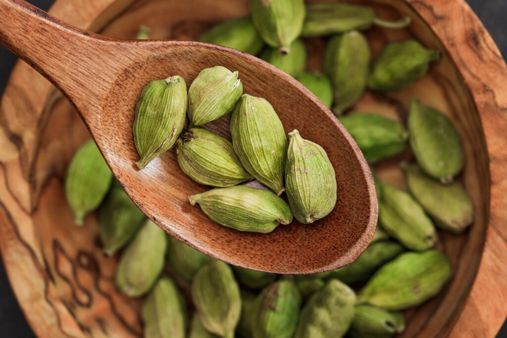 Wooden spoon holding fresh green cardamom on rustic bowl. Ideal for culinary themes.
